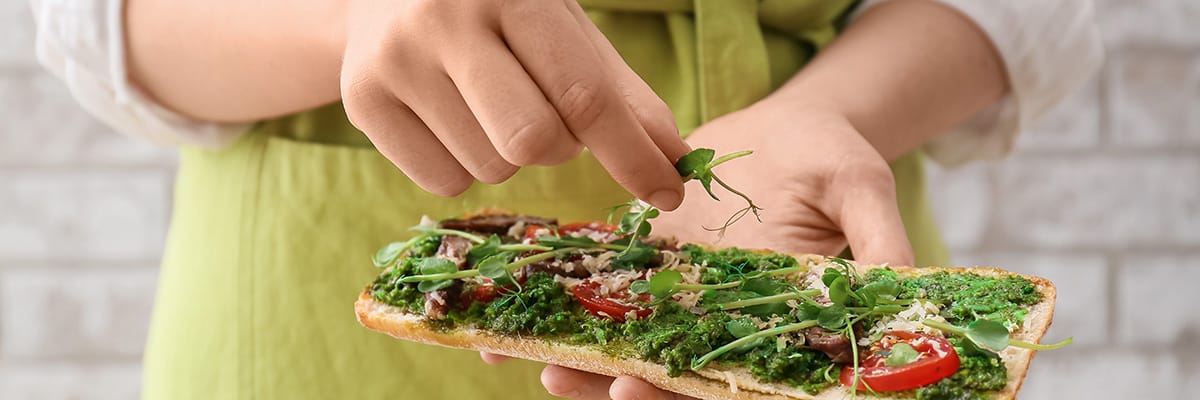 Person adding fresh herbs to a deliciously prepared flatbread, showcasing a focus on flavor and presentation