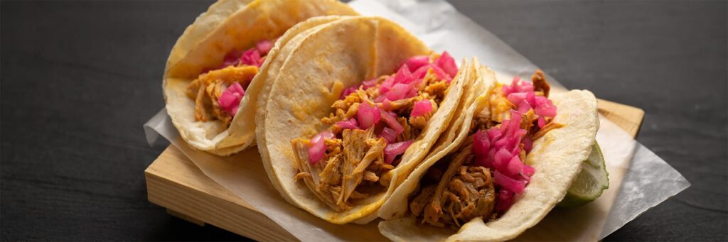 Three delicious tacos filled with seasoned meat and topped with pink onions, served on a wooden platter