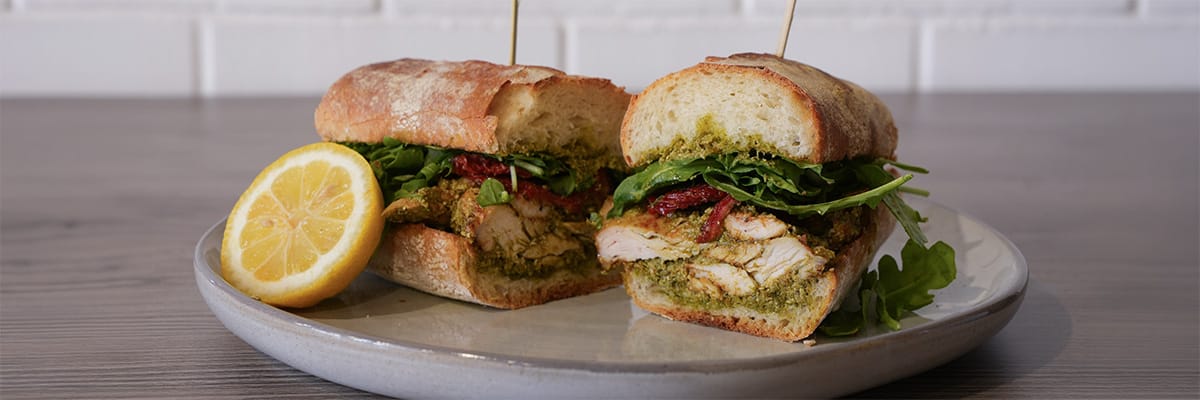 Delicious sandwich filled with chicken, pesto, sun-dried tomatoes, and arugula, served with a lemon wedge