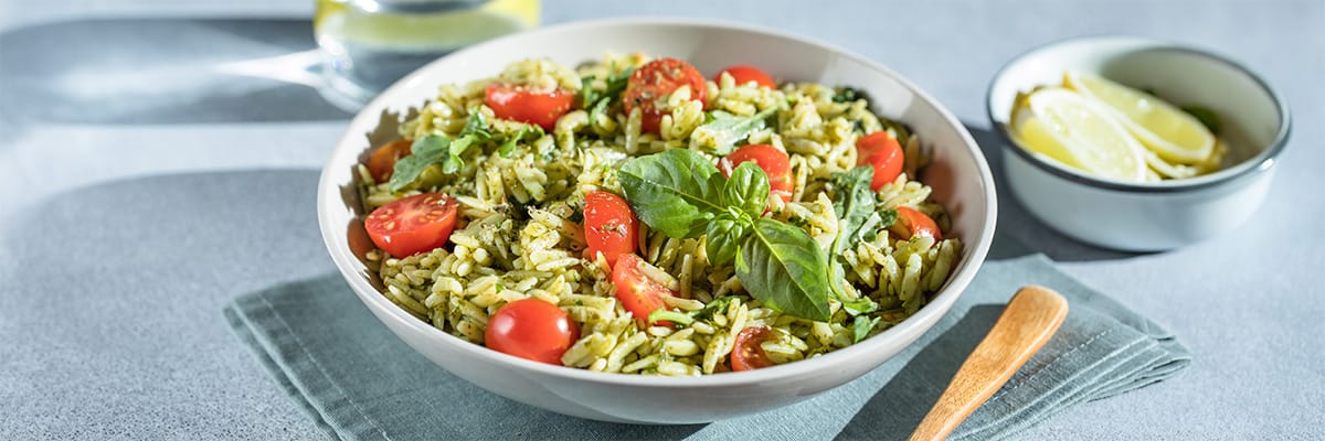 Bowl of delicious pesto rice with cherry tomatoes and fresh basil, served with lemon wedges on the side