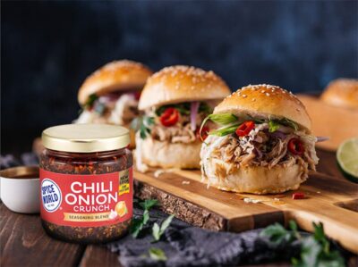 Burgers topped with fresh ingredients, paired with Chili Onion Crunch seasoning on a wooden board
