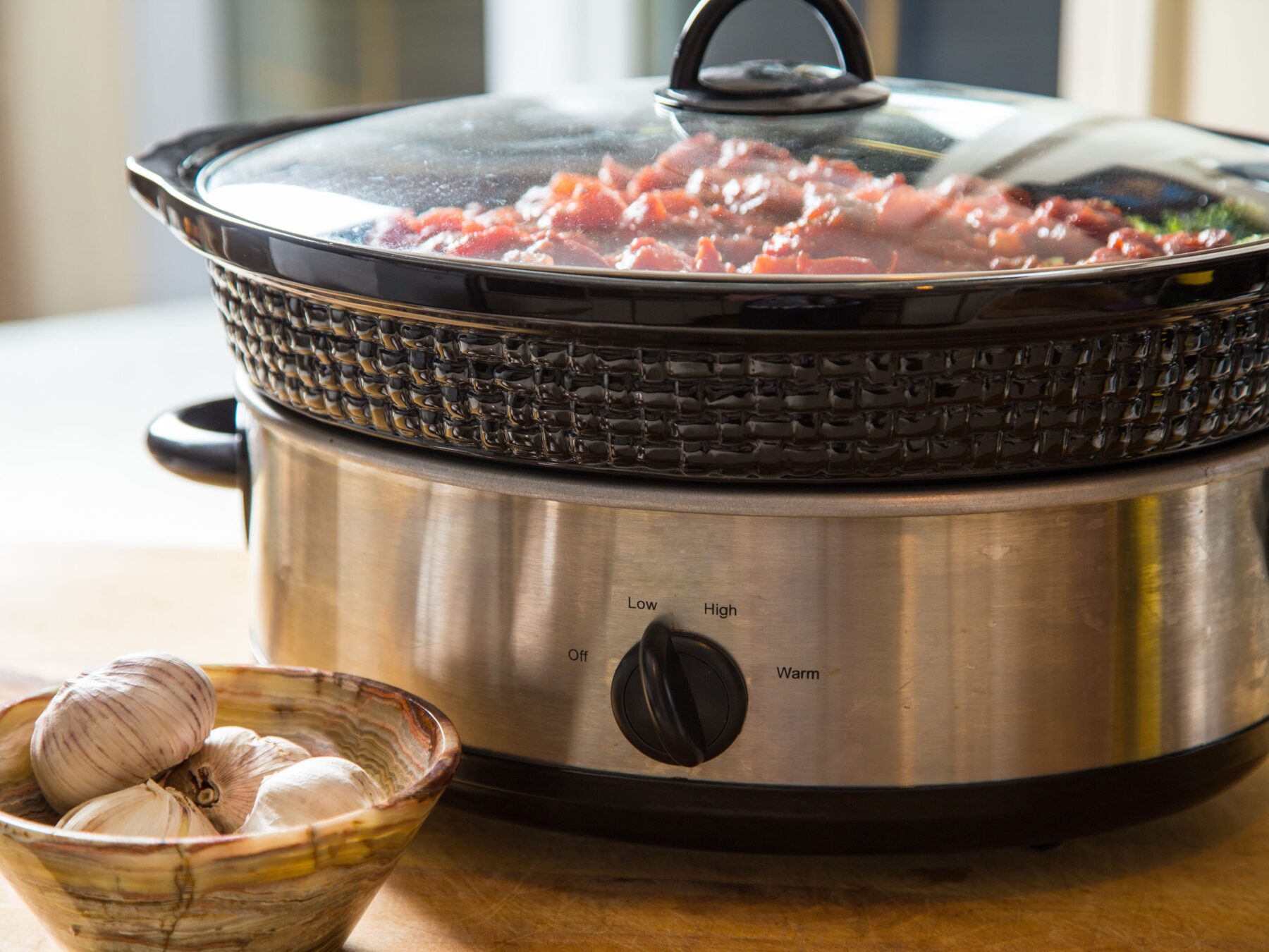 Slow cooker with simmering ingredients beside a bowl of garlic, highlighting a delicious meal preparation