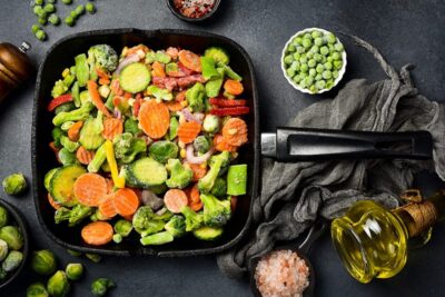 Skillet with colorful mixed vegetables, ready for a delicious meal, surrounded by seasoning and olive oil